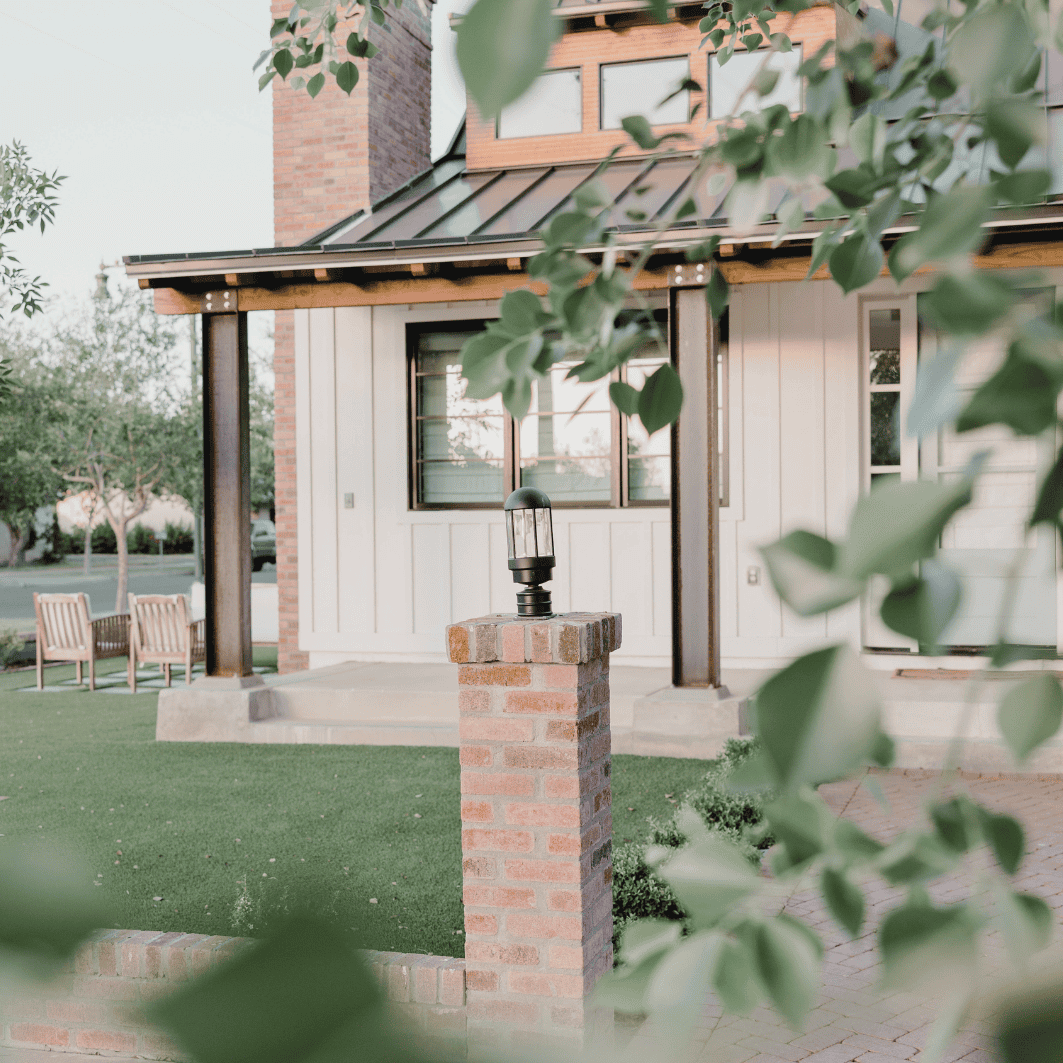 Modern house with brick and wood exterior, outdoor lighting, and lush greenery.